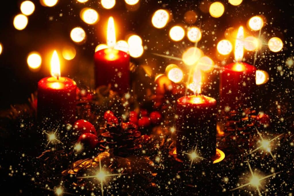 Vier rote Kerzen werden zwischen Tannenzapfen und festlichen Dekorationen angezündet, umgeben von warmen, leuchtenden Lichtern und funkelnden Effekten, die eine gemütliche Weihnachtsatmosphäre schaffen.