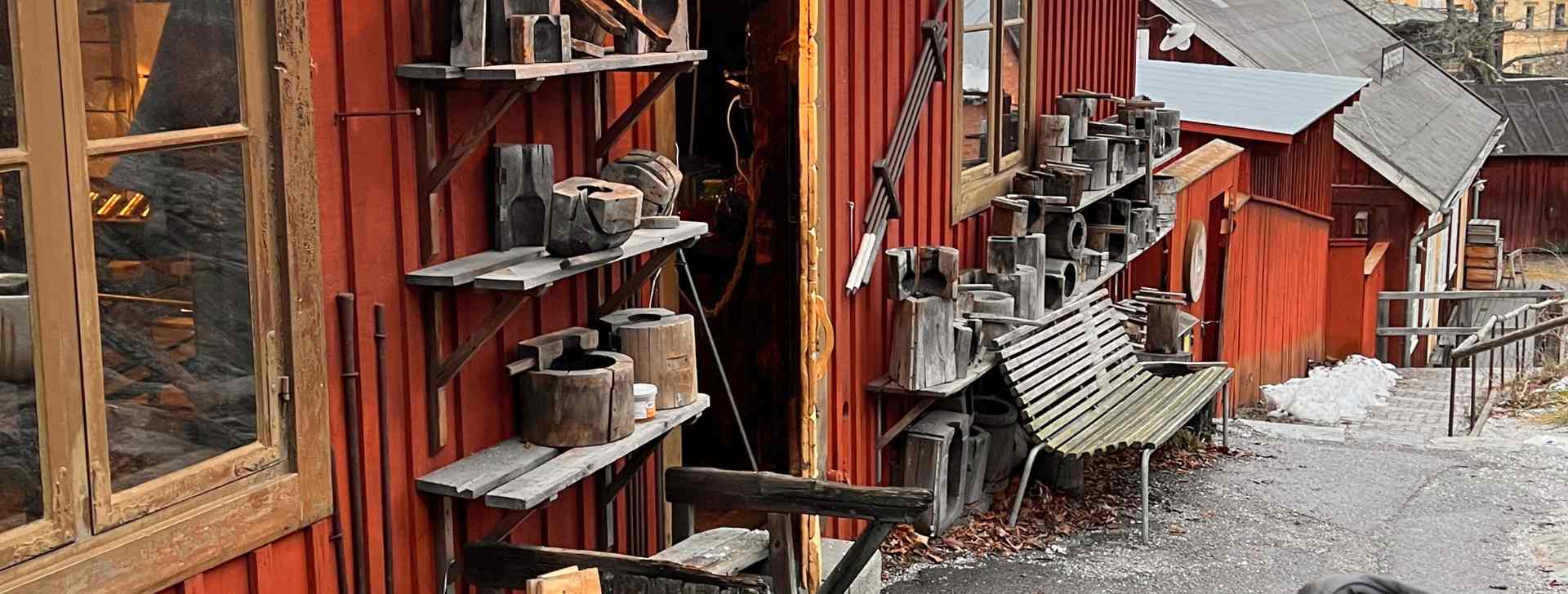 Eine Häuserzeile im Freilichtmuseum Skansen, rote Holzhäuser mit Werkzeug und Bänken vor den Häusern