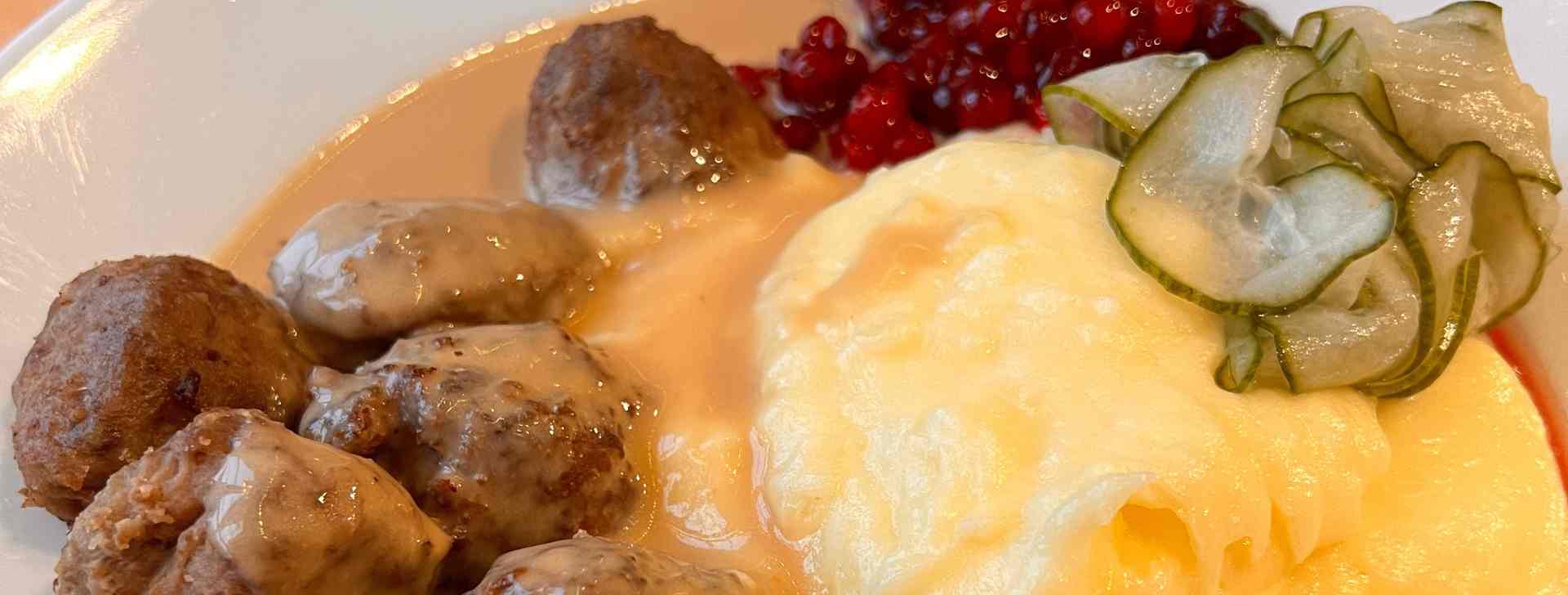 Ein Teller mit Köttbullar (schwedische Fleischbällchen) Erdäpfelpüree, eingelegte Gurken und Preiselbeeren