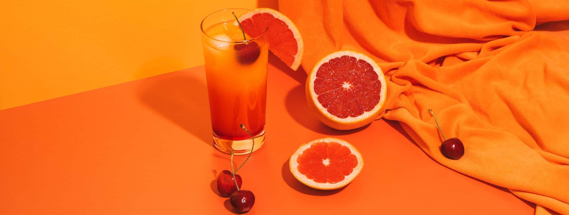 Ein Tisch von oben fotografiert, auf dem Tisch ist ein Glas mit Orangensaft und Orangen